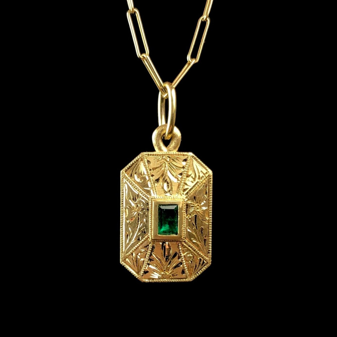 Front view of gold rectangular pendant with green emerald in the center