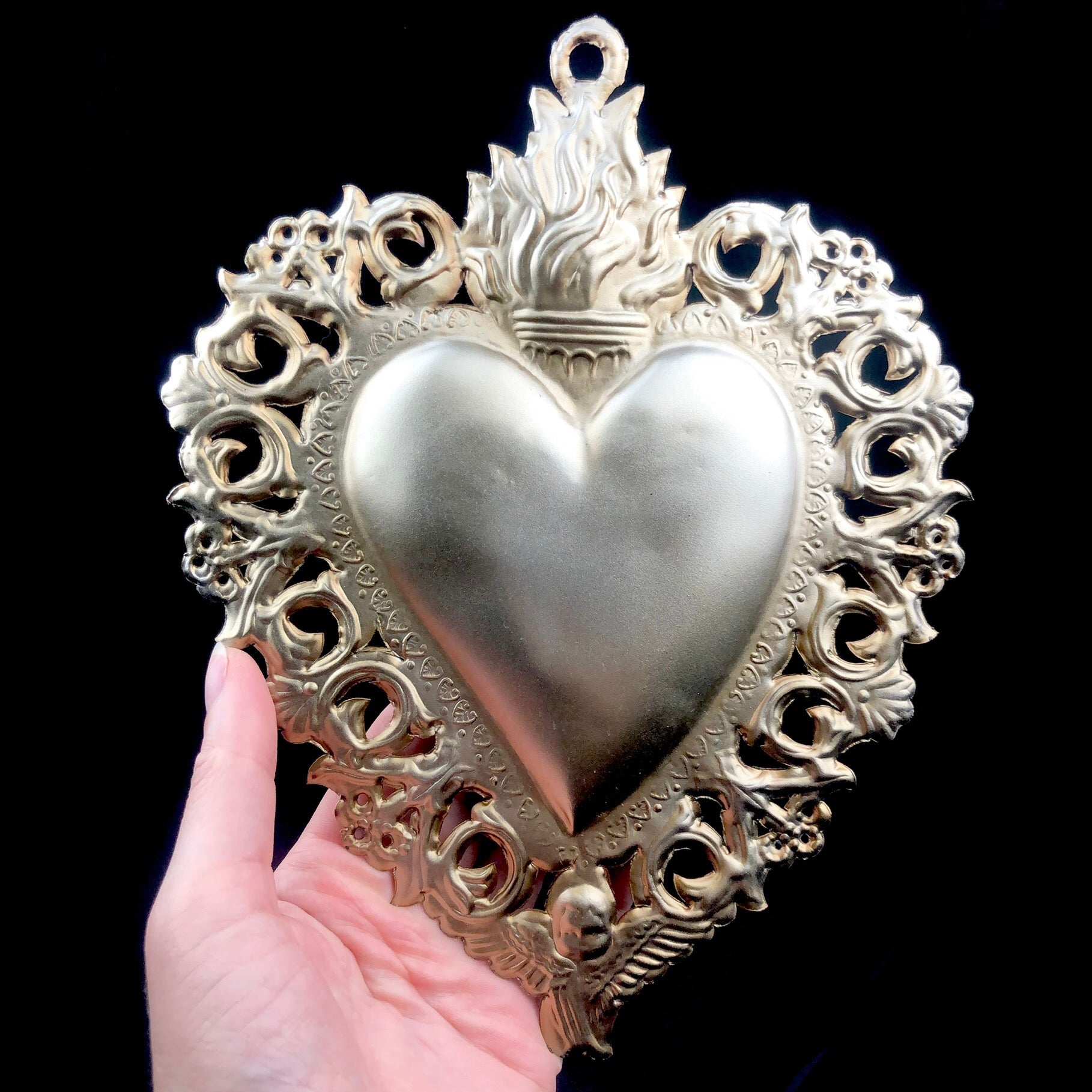 Silver sacred heart with cutout lace boarder shown in hand