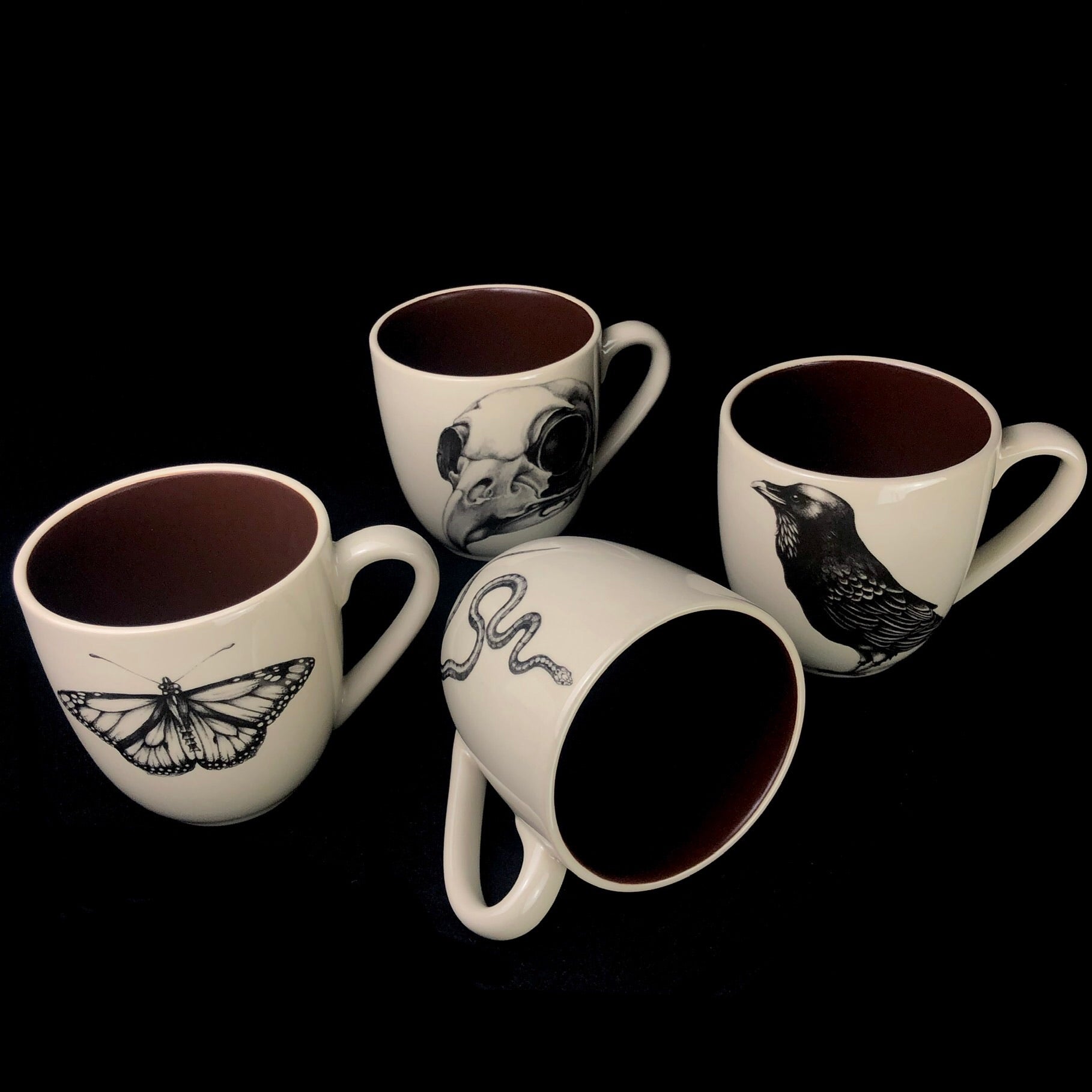 Set of four mugs with drawings referencing death including the Monarch Butterfly, Snake, Raven and Owl Skull